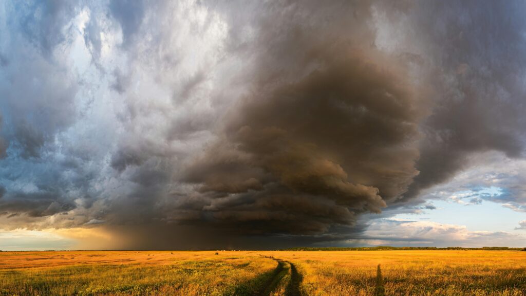 Expansive field under dramatic storm clouds with sunlit landscape, showcasing nature's power.